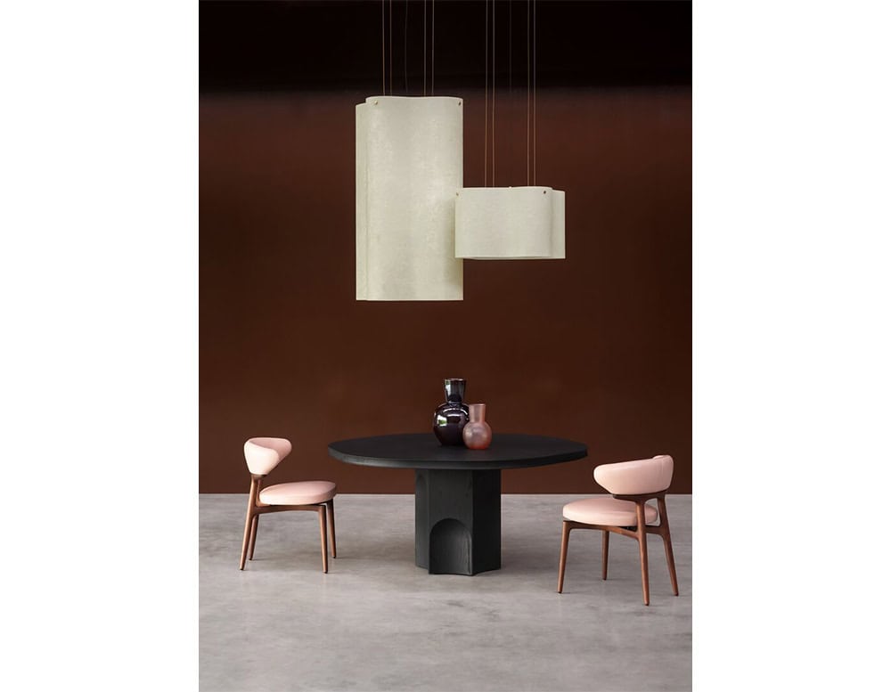 The Bax Clotilde Chair adds a soft, modern touch with its blush seat and sculpted wood frame. Paired with a bold round table and minimalist lighting, it creates a sophisticated dining setting.