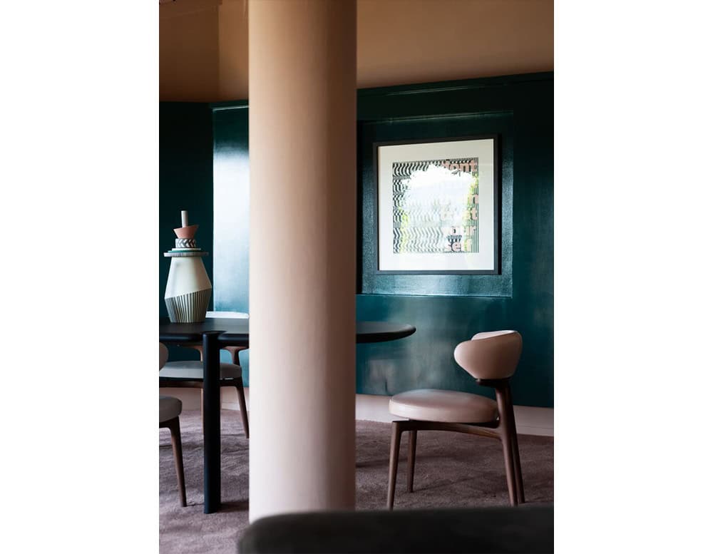 The Bax Clotilde Chair introduces soft curves and warm tones, blending seamlessly into a refined dining space with sculptural decor and rich emerald walls.