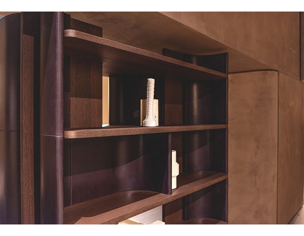 This close-up captures the Bax Joni bookcase, highlighting its dark wood finish and sculptural side panels. Minimal ceramic objects are placed along the shelves, drawing attention to the contrast between the materials.