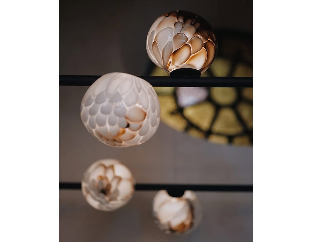 The Boc 118 Series pendant lights feature hand-blown glass spheres with warm amber and white tones, creating a rich, organic texture along slender horizontal rods.