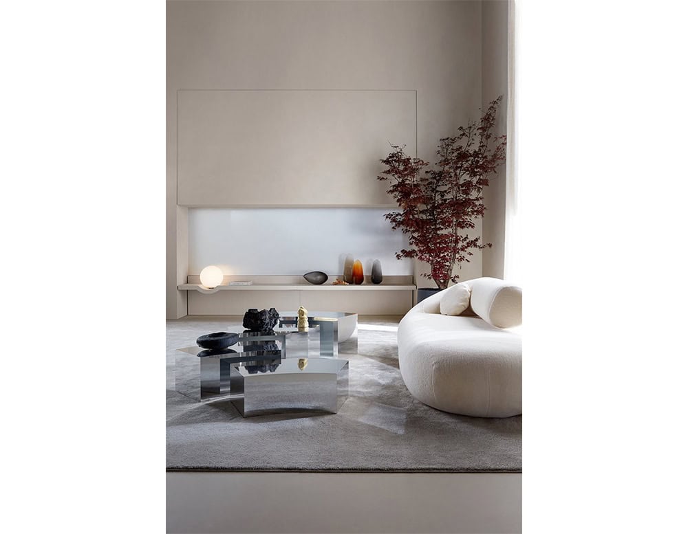 Mirror-polished stainless steel coffee tables create a reflective centerpiece, adding geometric contrast to the soft, neutral-toned living room arrangement.