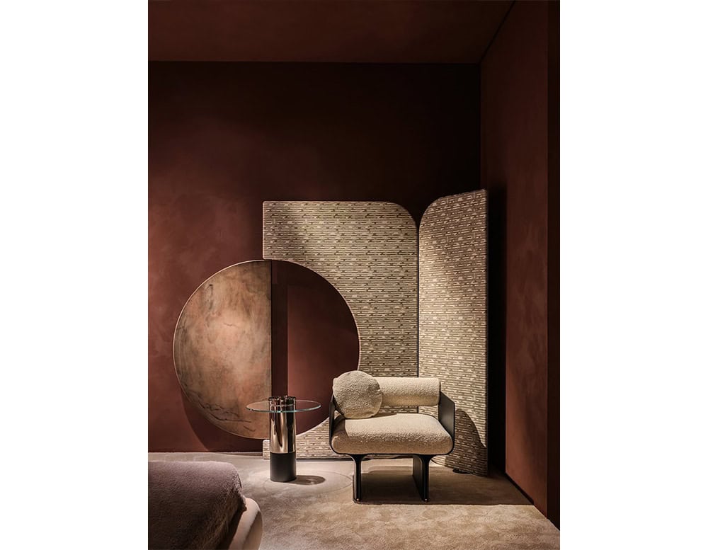 The Enso Screen features curved panels with a textured surface in light neutral tones, creating a soft geometric backdrop. Its layered form adds depth to the room, complemented by minimal furniture with warm beige and taupe hues.