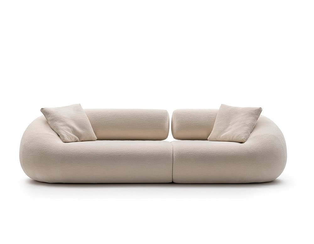 An Evolis Next Sofa in a subtle light tone, featuring plush cushions and rounded contours. Two casual throw pillows complement its relaxed, contemporary design, enhancing its cozy appeal.