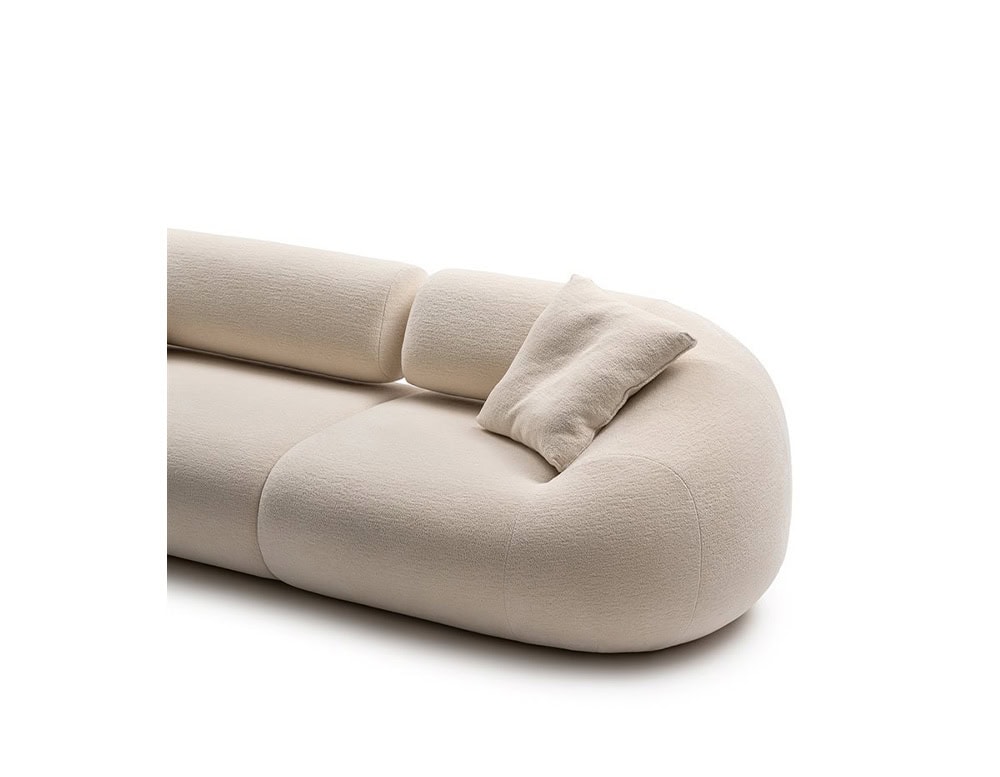 An Evolis Next Sofa with plush, rounded forms and a smooth, light-toned fabric. A casually placed pillow rests on the backrest, emphasizing the piece's relaxed and inviting design.