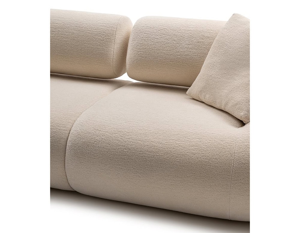 A close-up of the Evolis Next Sofa, emphasizing the seamless curves of its plush seat and cylindrical backrest. The upholstery is in a light, neutral tone, complementing the sofa’s soft and inviting texture.