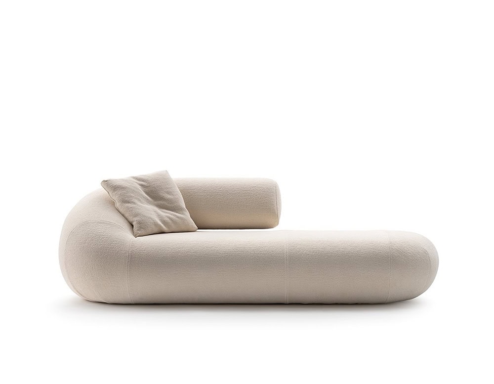 An Evolis Sofa module featuring a gently curved backrest and rounded seat profile. The piece is upholstered in a light, soft fabric and includes a casually placed cushion in a similar tone, adding a relaxed, plush detail.
