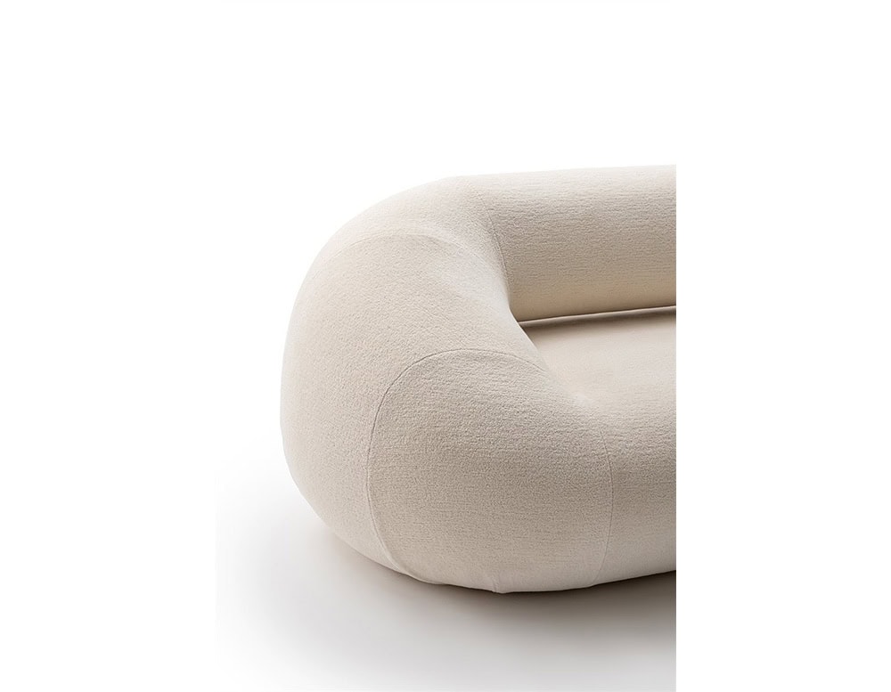 A close-up of the Evolis Sofa’s arm and seat corner, highlighting its sculptural, rounded form. The fabric upholstery appears soft and light-toned, emphasizing the piece's smooth, continuous curves and seamless stitching.