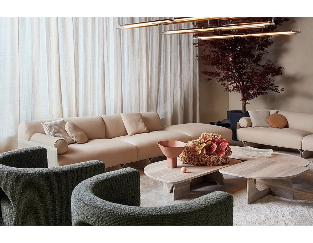 A warm interior composition with the GR H2O Lounge Chairs, softly textured and curved, positioned around pale wood coffee tables. Neutral and earthy seating elements complete the calm, inviting lounge setting.