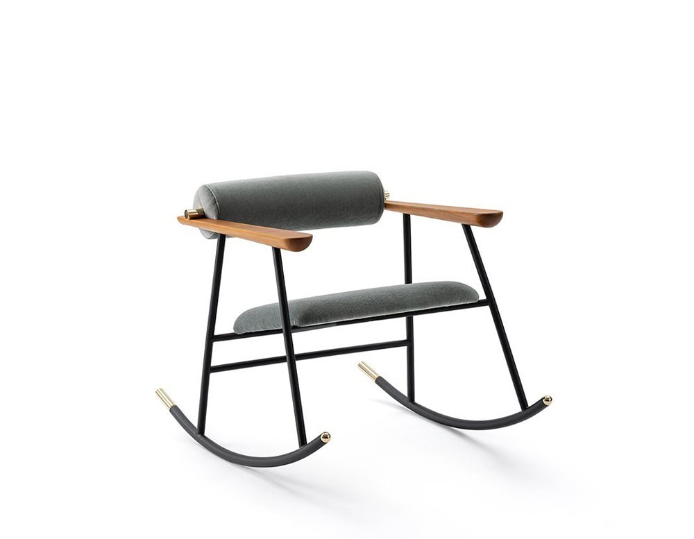 Lou Lou Rock Chair in a sophisticated mix of materials, featuring grey upholstery, warm wooden armrests, and a matte black frame. Brass details accent the sleek curves, set against a clean white background.