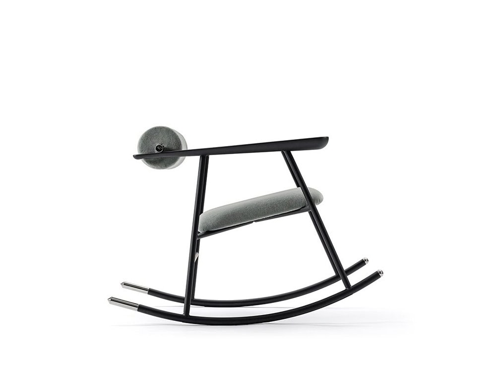 Lou Lou Rock Chair in a sleek side profile. The chair showcases a matte black frame with soft grey upholstery and brass-capped rocking legs, set against a clean white background.