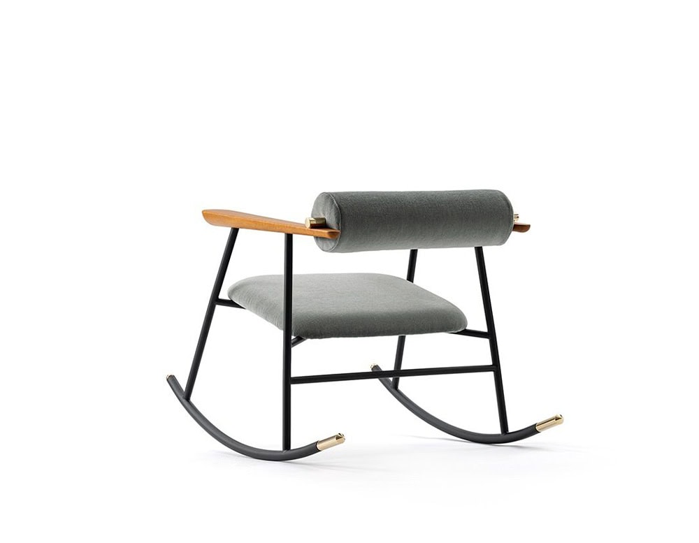 Lou Lou Rock Chair in a side angle view. It features a matte black frame, grey cushioned seat and backrest, and warm wood armrests with brass detailing on the rocker ends, set against a white background.