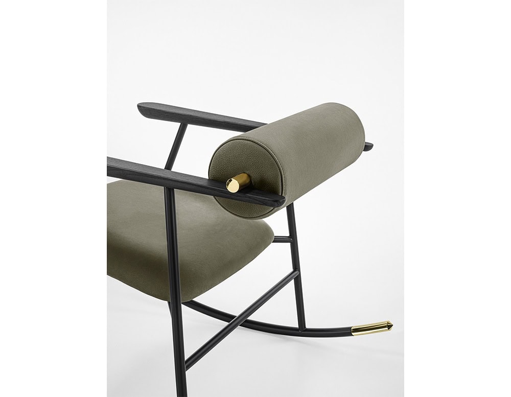 Lou Lou Rock Chair detail view. The close-up captures the olive green seat and backrest, the black ash wood armrest, and the polished brass rod securing the cylindrical back cushion.