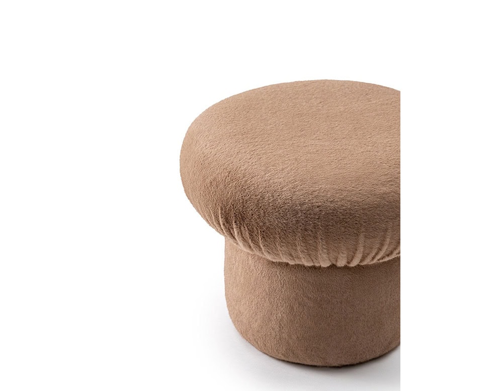 The GR Nala Stool, in a soft taupe tone, features a rounded cushion and cylindrical base. Shot against a white background, the close-up highlights its inviting texture and playful, plush design.
