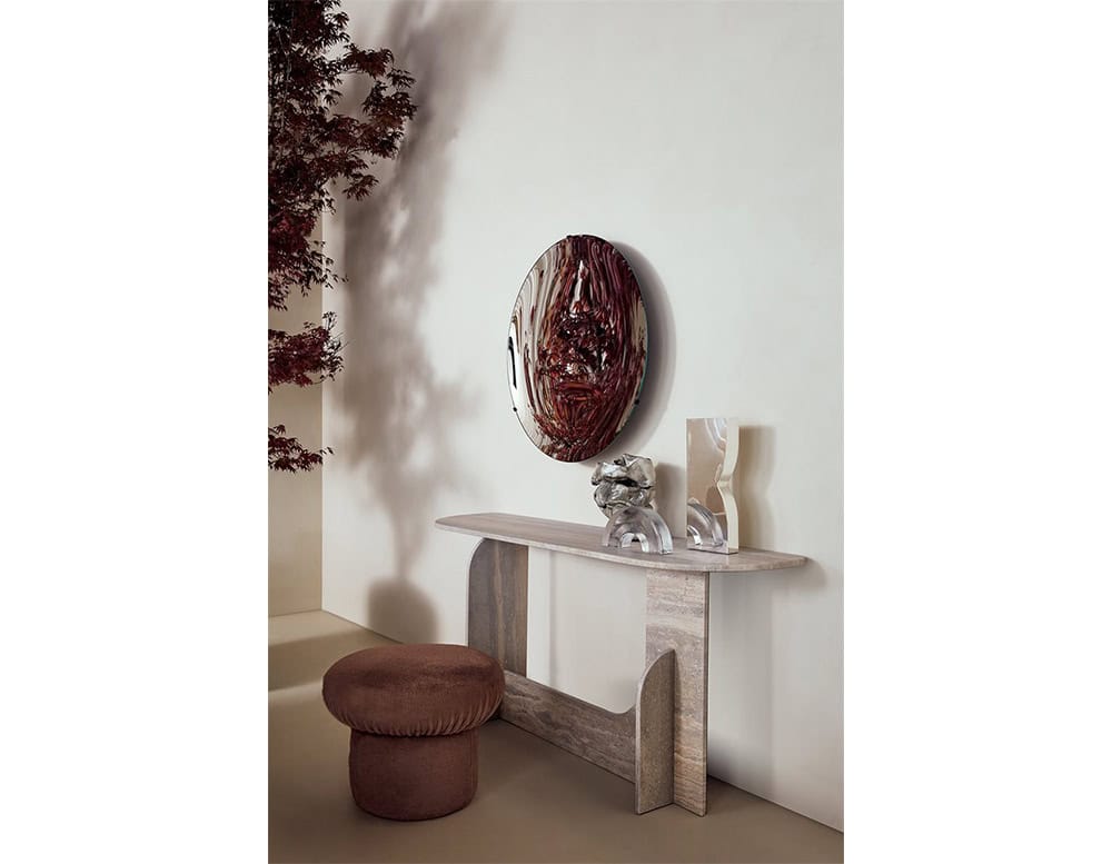 GR Nala Stool in rich brown velvet is placed in a refined interior. It sits beside a stone console and sculptural décor, under soft lighting that highlights its rounded, plush silhouette and cozy texture.