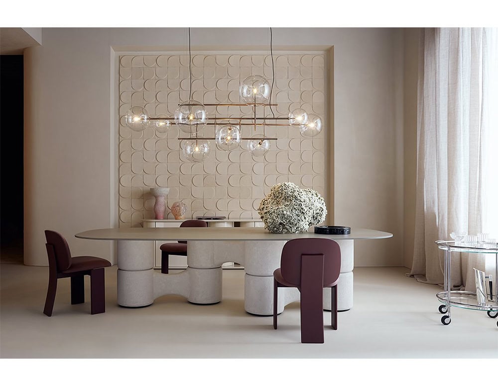 The GR Saki Chair adds sculptural elegance to a refined dining setting, with deep plum upholstery and architectural wood bases that complement the room’s geometric textures and warm neutral palette.