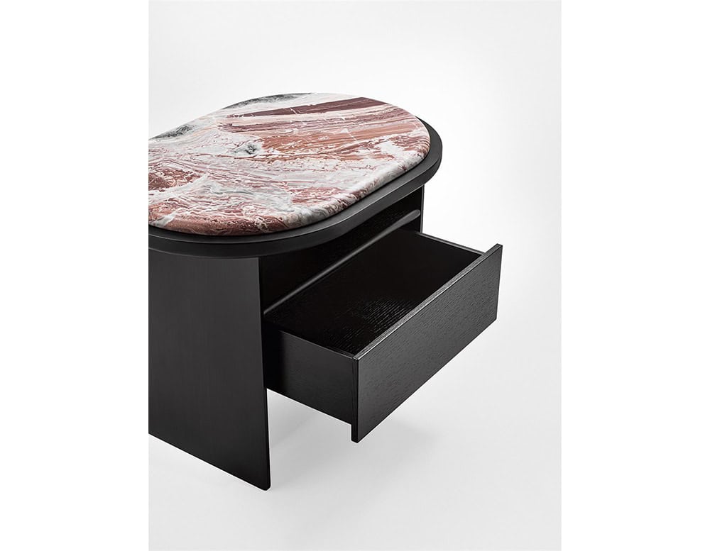 The GR Sensei Night Table reveals a softly rounded top in marbled tones of rose and ivory. Its black wood frame integrates a smoothly sliding drawer, offering discreet storage beneath the elegant surface.