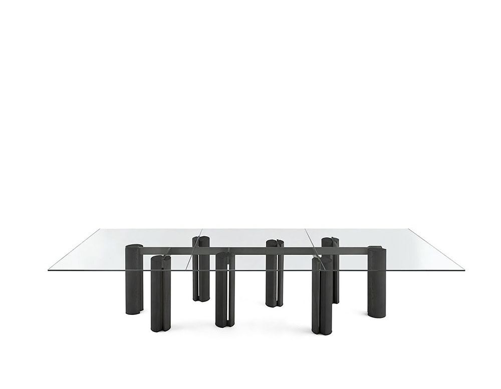 The GR Simpodio System W Coffee Table features a sleek glass top over modular dark wood bases. The composition is minimal, set against a white background to emphasize its linear form.