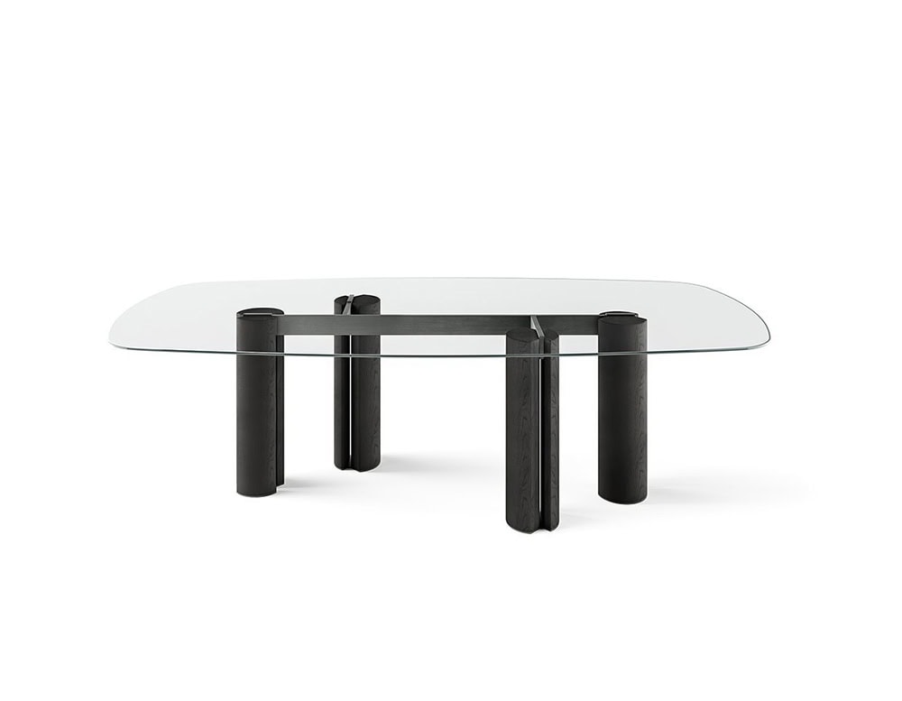 The GR Simpodio W Table highlights a minimalist structure with a clear glass top that floats over bold cylindrical legs. The transparent surface reveals the deep charcoal base, giving the piece an airy yet grounded elegance.