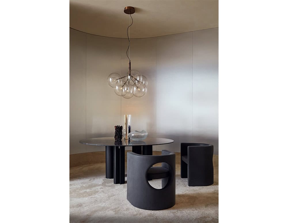 The GR Simpodio W Table anchors the space with a smoked glass top and bold base. Paired with rounded chairs and neutral tones, the scene feels quiet and sculptural.