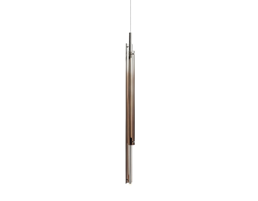 The GR Tratto Suspension Light displays a sleek vertical arrangement with soft bronze tones. Its transparent glass and polished metal finish produce a delicate shimmer, adding sophistication without overwhelming the space.