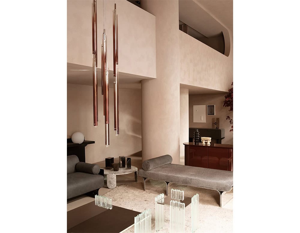 The GR Tratto Suspension Light cascades from the ceiling in slender, vertical forms. Its warm bronze tones reflect softly against the neutral interior, creating an elegant yet subtle focal point in the living space.