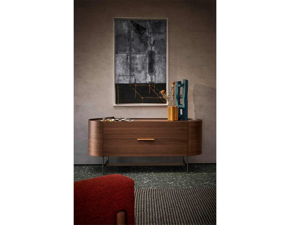 The Pian Dedalo Nightstand in warm wood finish features smooth curves and minimal lines, elegantly styled with sculptural decor and modern artwork in a refined interior setting.
