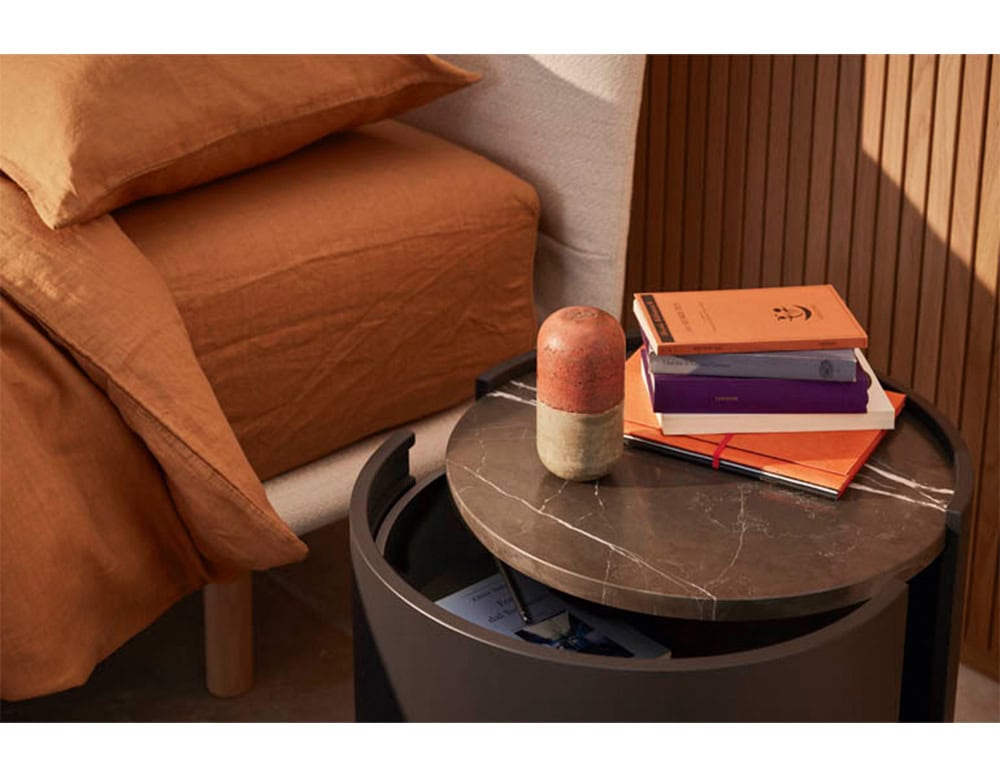 The Pian Dedalo Nightstand features a marble top and discreet curved storage, blending elegant materials with smart functionality beside a warm and relaxed bedroom setup.