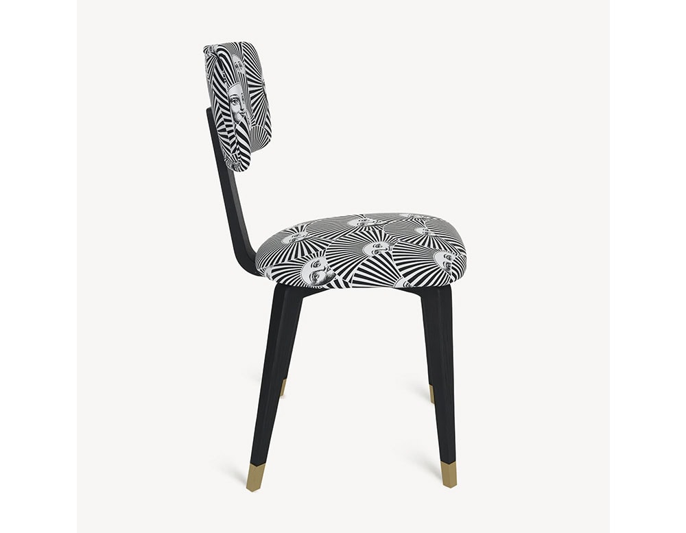 The Fornasetti Soli a Ventaglio Chair displays a dynamic radial sun face print in black and white. Its sleek black frame is accented with brass-detailed feet for a refined finish.