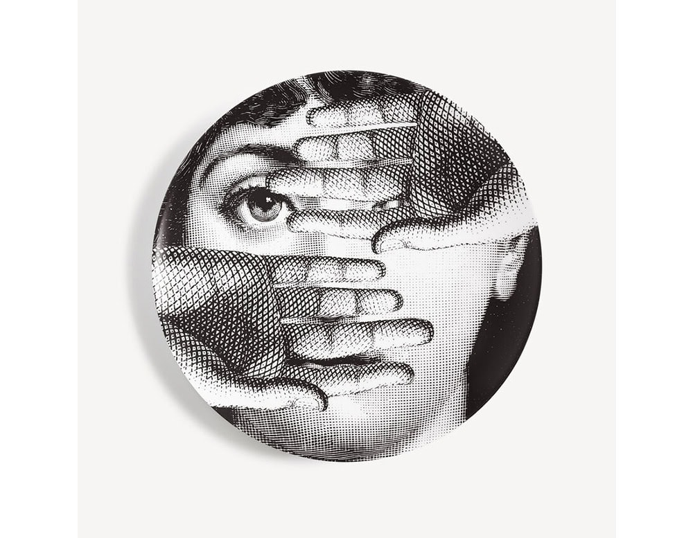 A striking black and white porcelain plate showcasing a woman's face partially obscured by layered hands. The surreal composition evokes intrigue and mystery making it a captivating decorative object or wall piece.