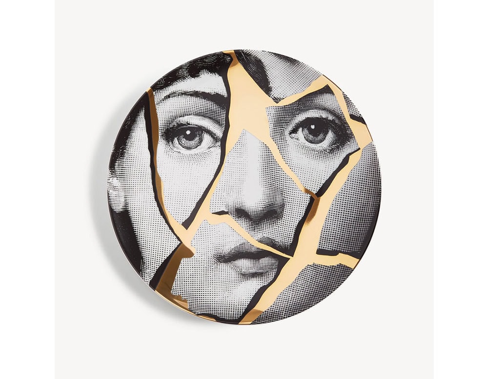 A striking decorative plate portraying a fragmented female face reassembled with golden fissures. This visual nod to kintsugi celebrates imperfection and resilience, offering a bold statement piece full of poetic symbolism.