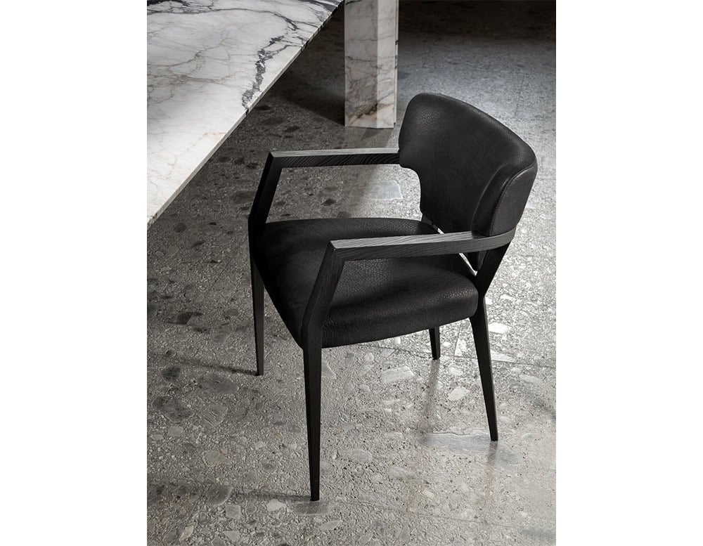 Hen Mantis Chair in black leather with a sculptural wood frame. The armrests extend with sharp precision and elegant angles, pairing effortlessly with the marble table shown nearby. Bold and minimal presence with refined detail.