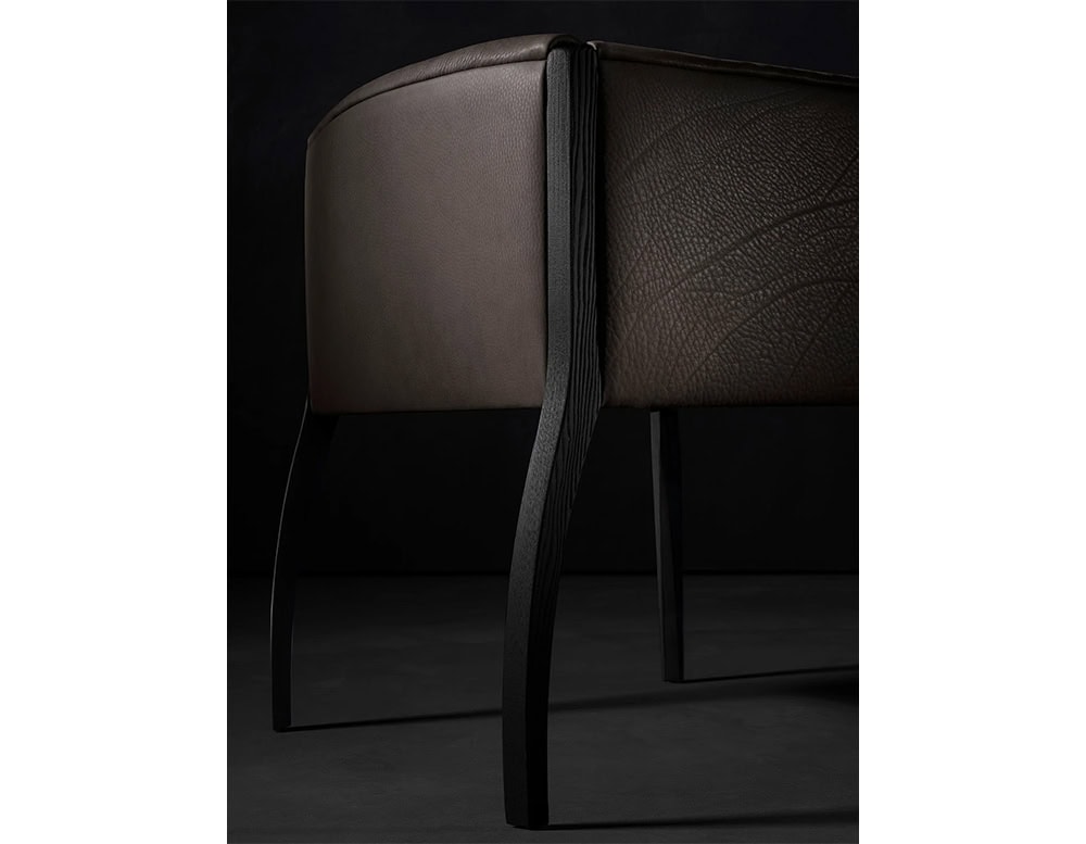 The Hen Shelly Chair highlights a gracefully curved back with textured leather and soft upholstery, supported by sculpted wooden legs that add a refined architectural presence.