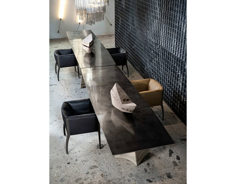 A sculptural dining table with a striking oxidized top and tactile base. The commanding presence is softened by subtle textures and rich materials, blending art and function into a singular design statement.