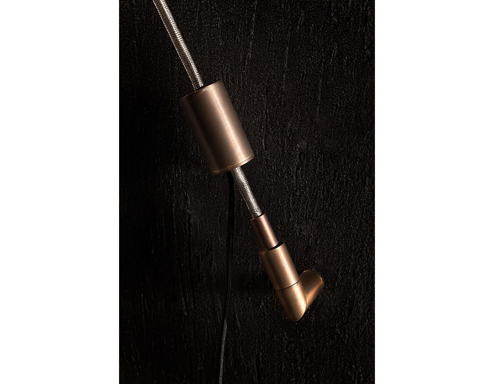 Detail of the Hen Spyder wall light shows a bronze-toned cylindrical fixture securing the braided cable with a precision-crafted angled support for a refined and industrial finish.