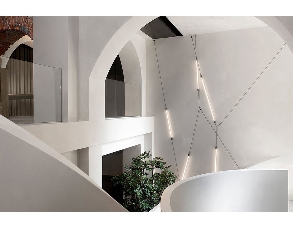 Hen Spyder Wall Light shown in an architectural installation with slim light rods suspended diagonally across a tall wall using tension cables to create a sculptural and rhythmic visual effect.