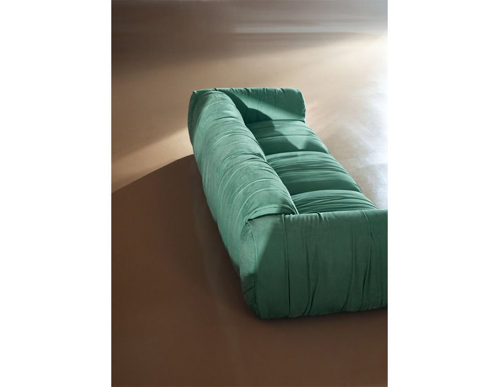 Contemporary green sofa featuring soft ruched fabric and wide cushions, styled in a warm-toned interior with natural light casting soft shadows.