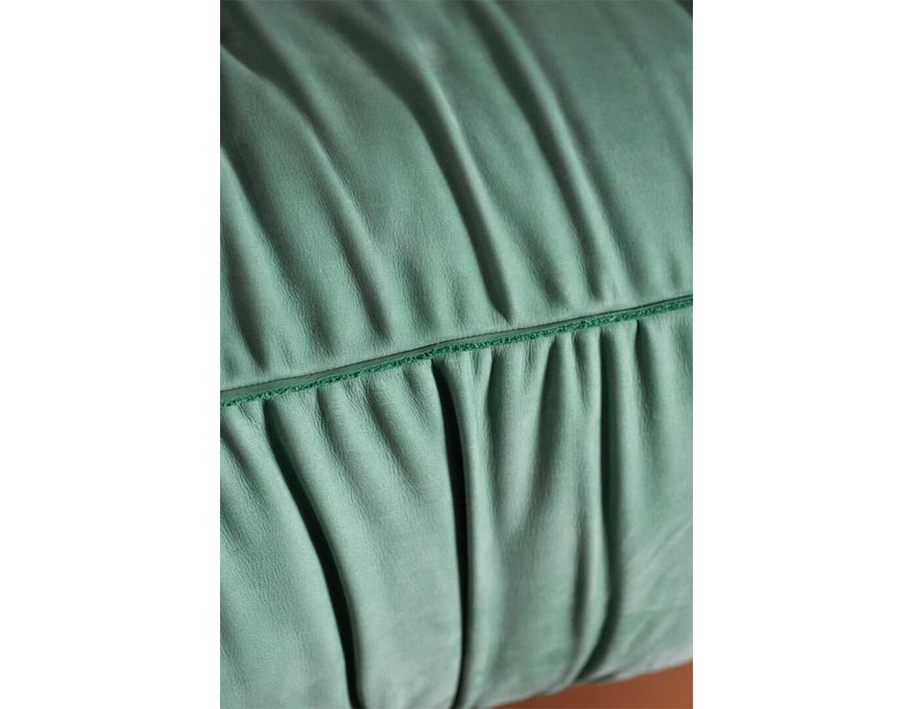 Detailed shot of soft green fabric upholstery with ruched folds and a stitched seam, highlighting the craftsmanship and tactile quality of the cushion.