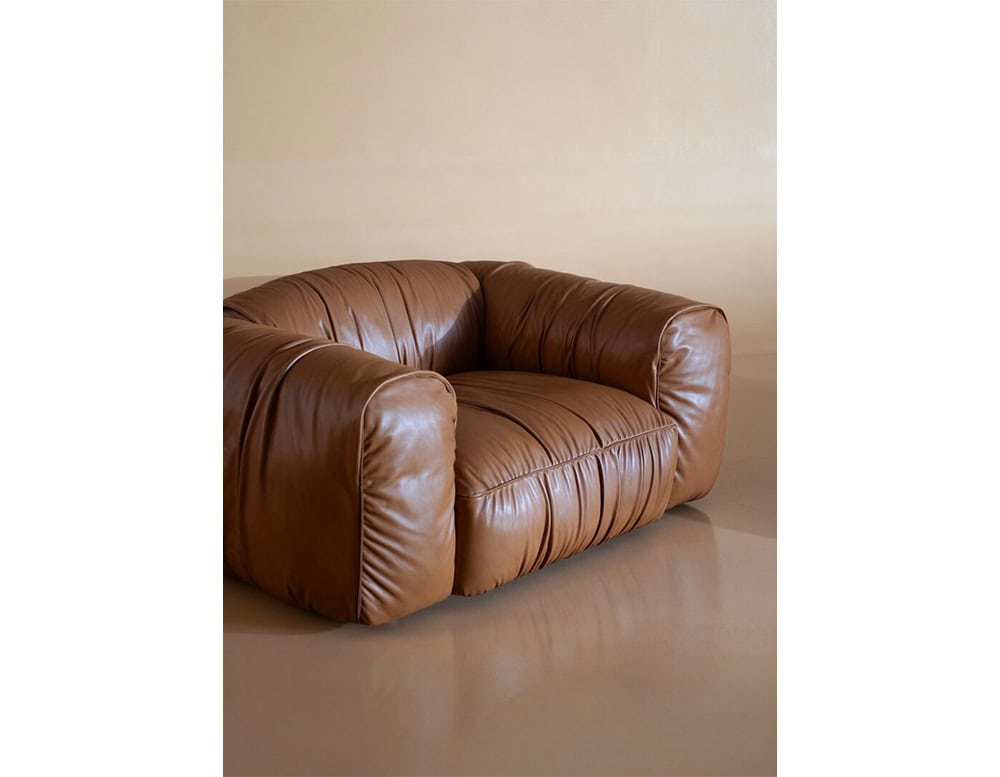 Plush brown leather armchair with a relaxed silhouette sits against a neutral backdrop, illuminated by warm sunlight that emphasizes its rich material and contemporary design.