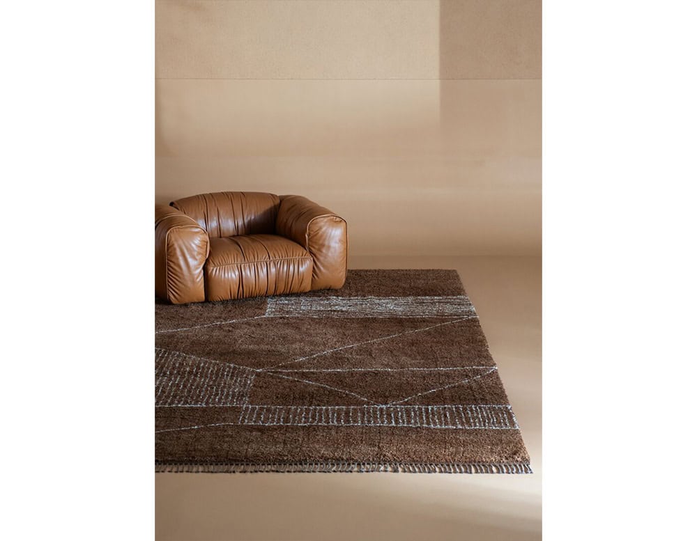 Contemporary lounge space featuring a low brown leather armchair paired with a textured brown rug with subtle geometric designs, creating a modern and inviting atmosphere.