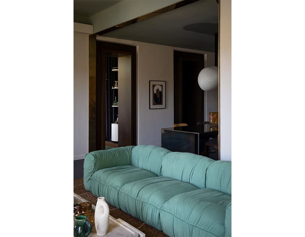 Modern interior featuring a plush green sofa paired with a marble coffee table with vases completes the space, accented by warm mustard walls and natural light.