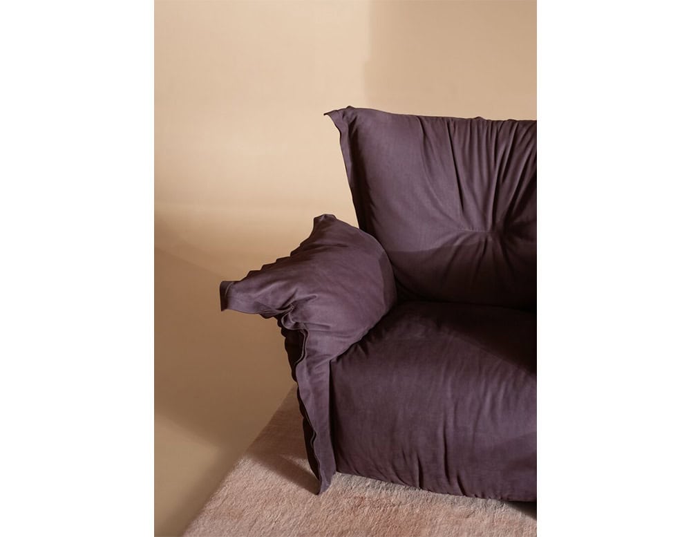 Deep purple armchair with oversized cushions and soft fabric upholstery, styled with relaxed seams and plush padding for a cozy seating experience.