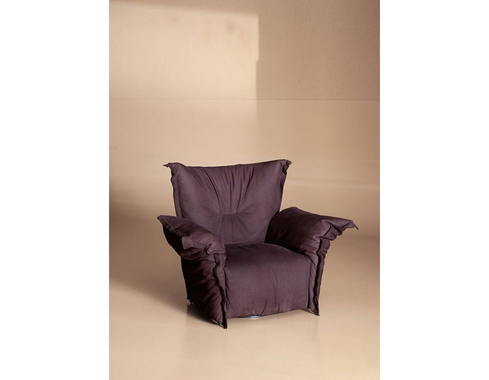 Deep purple armchair with oversized cushioned arms and a relaxed silhouette, set against a neutral-toned backdrop for a cozy yet refined seating statement.