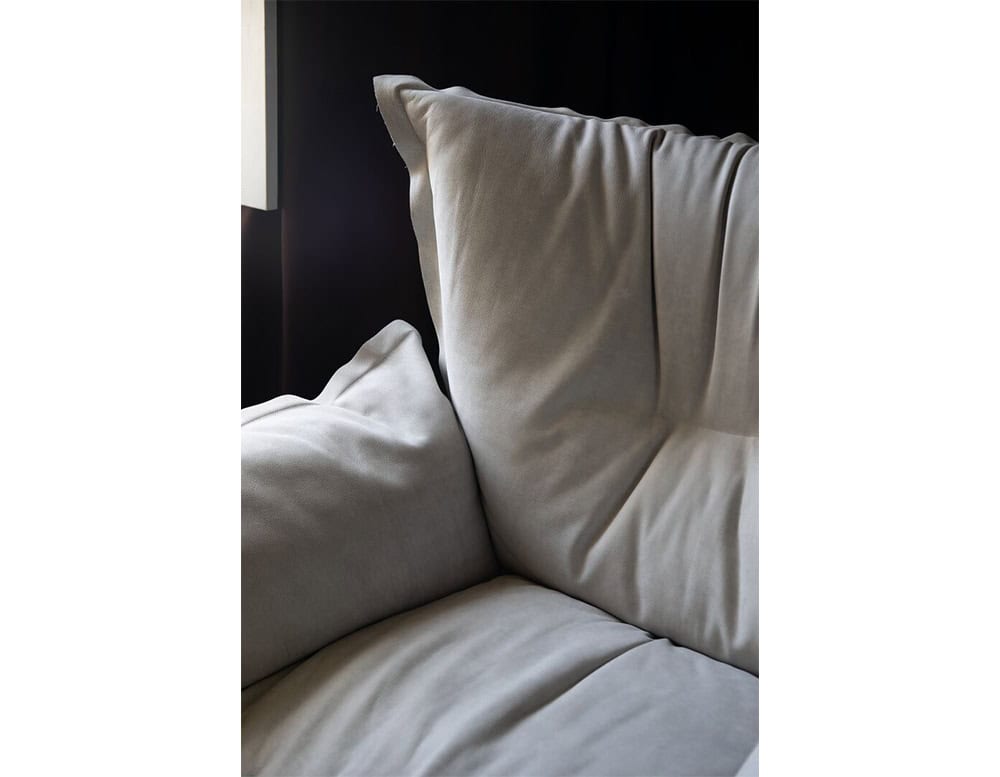 Detailed view of the armchair showcasing its plush grey fabric and deep cushions emphasizing comfort and contemporary style in a soft light.