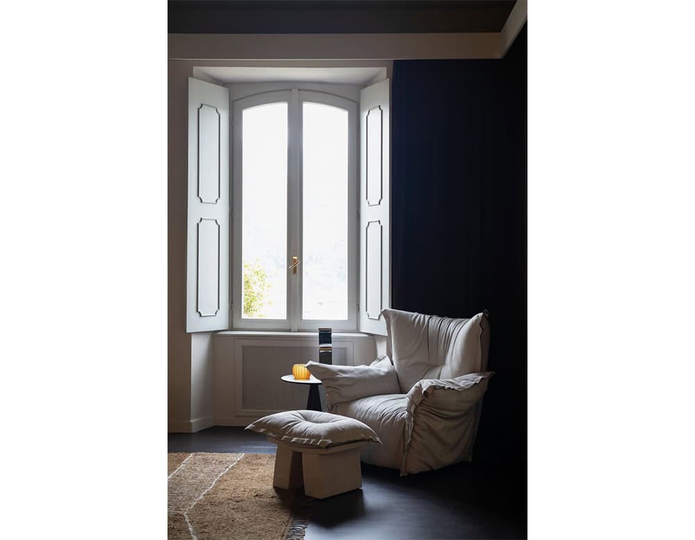 A cozy reading corner with a soft armchair and matching ottoman placed by a large window letting in natural light and creating a serene atmosphere.