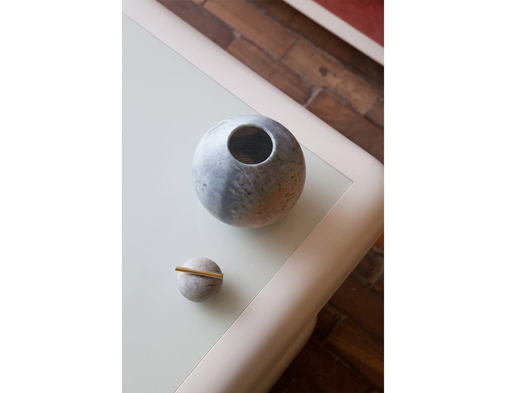 AOI Vase features a rounded stone form with smooth natural texture and a refined brass accent on its lid creating a sculptural piece with timeless elegance.