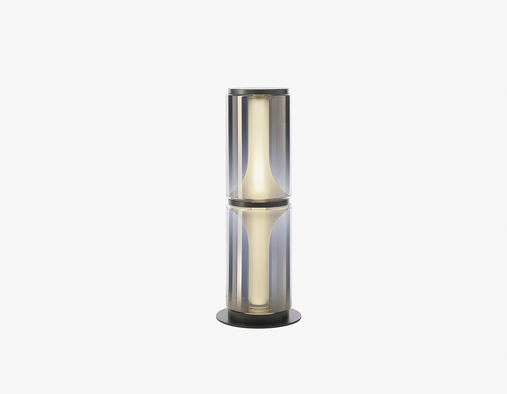A compact floor lamp with two smoked glass cylinders and soft diffused light, offering a modern sculptural touch for intimate and stylish spaces.