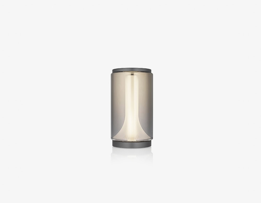 A single smoked glass cylinder lamp with a soft diffused glow, perfect as a minimalist accent light that adds a refined and contemporary touch to interiors.