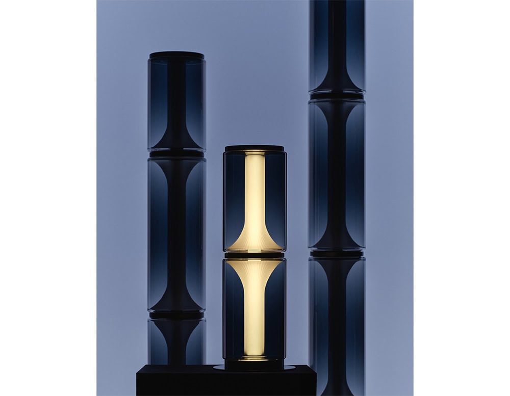 Las Miles Lighting features deep smoked glass cylinders with a glowing warm core, creating a striking contrast of light and shadow that elevates modern interiors.