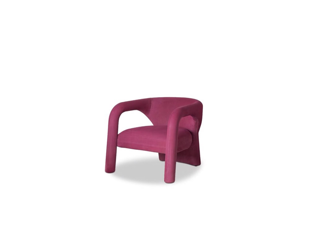 A sculptural armchair in bold magenta velvet, defined by fluid, rounded lines and an embracing form that balances modern artistry with plush comfort.