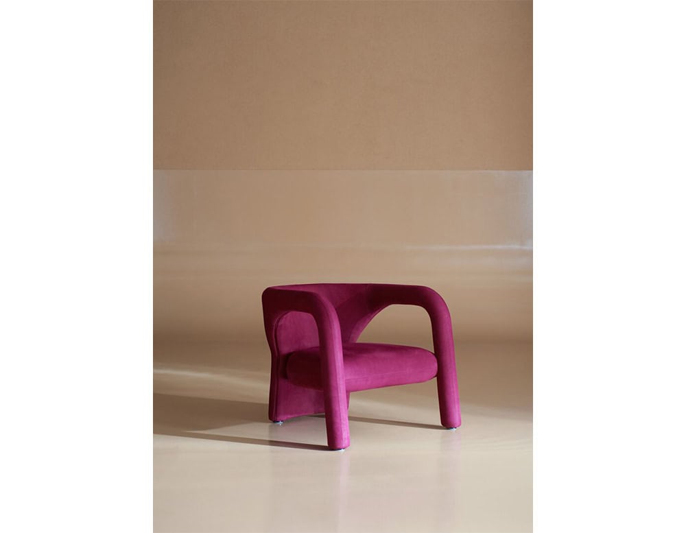 Contemporary magenta armchair featuring soft curves and an enveloping silhouette, combining bold color with refined comfort for a striking statement piece.